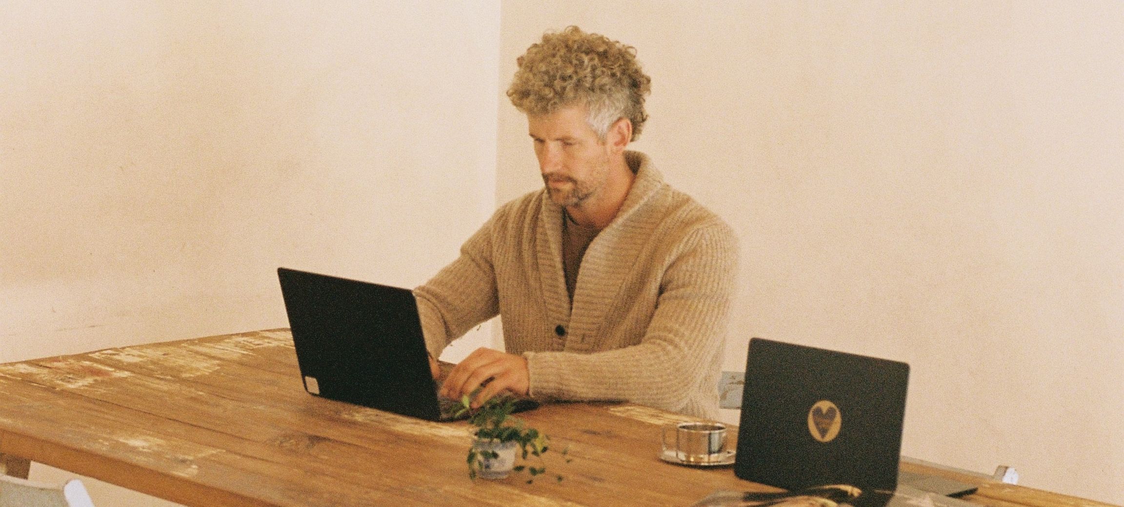 A member working on a laptop at the Bali table, built from an old wooden boat, with white folding chairs around it