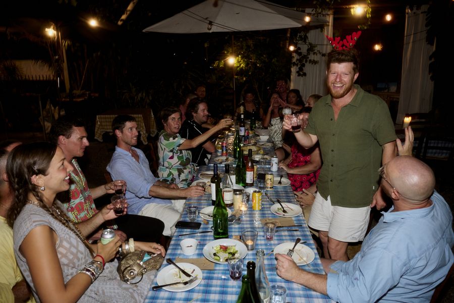 A smiling guest in red antlers stands with a raised glass while seated guests toast along the long table.